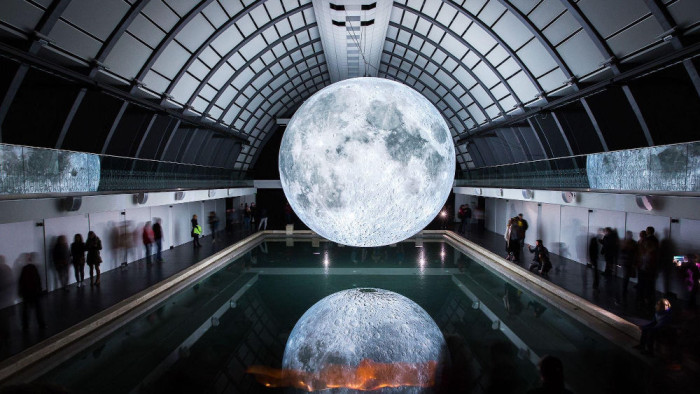 Photograph - a radiant moon hangs over a dark swimming hall, its luminous body reflected in the water.