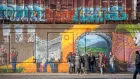 A small group of people in winter coats are clustered around outside a former industrial building covered in murals and graffiti.