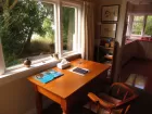 A polished wooden writer's desk sits beneath a window looking out onto green woodland.