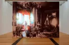 An artwork fills an exhibition space: a sepia photograph of a grand Regency-era room, in which hovers a young woman, in colour, like a kind of ghost.